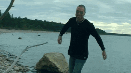a man in a black shirt is walking along a rocky beach