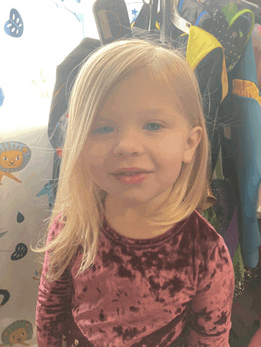 a little girl wearing a pink velvet shirt is smiling