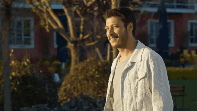 a man in a white jacket is smiling in front of a red house