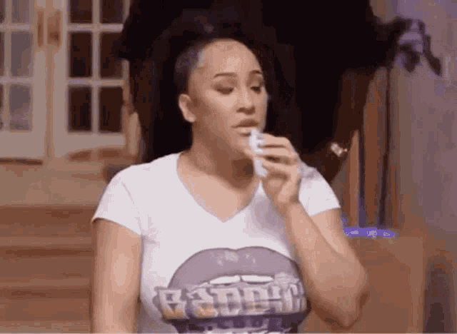 a woman in a white t-shirt with a purple lip is holding a napkin in her hand .