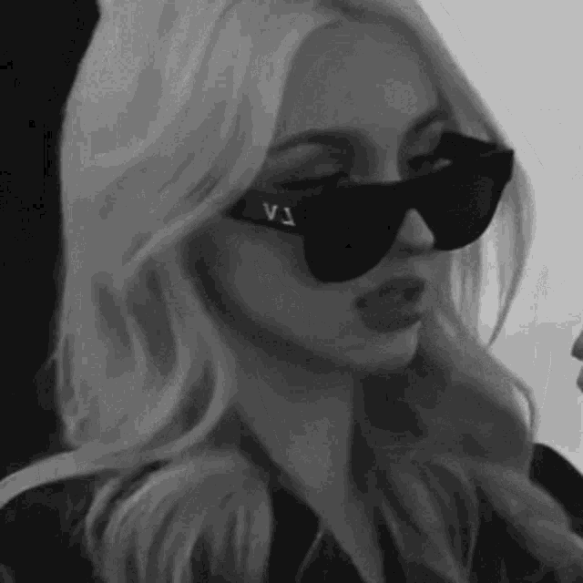 a woman is wearing sunglasses and a leather jacket in a black and white photo .