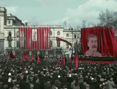 a large crowd of people are gathered in front of a red curtain with a picture of a man on it