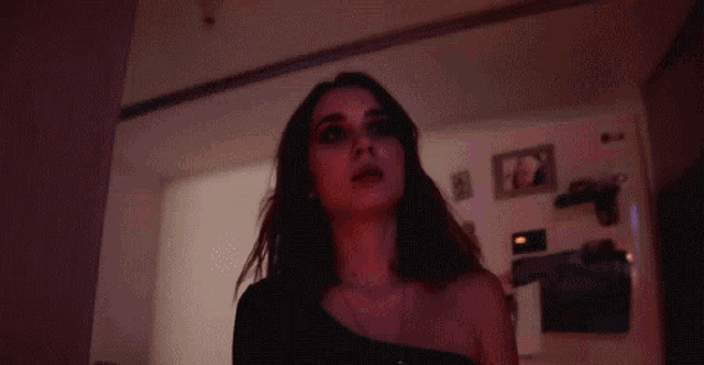 a woman in a black dress is standing in a dark room with a red light behind her .