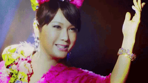 a woman in a pink dress with flowers in her hair is waving her hand .