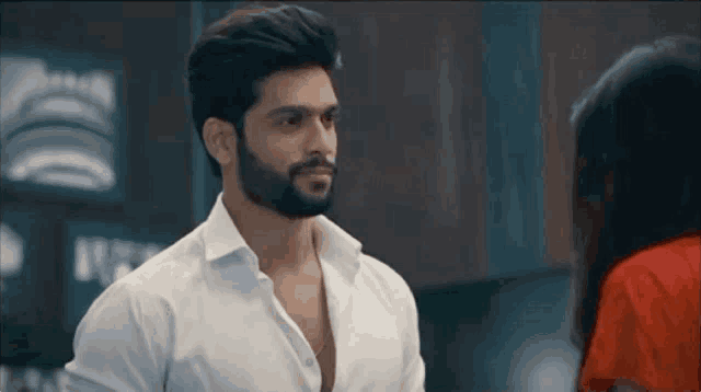 a man with a beard wearing a white shirt is looking at a woman in a red dress .