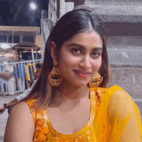 a close up of a woman wearing earrings and a yellow dress