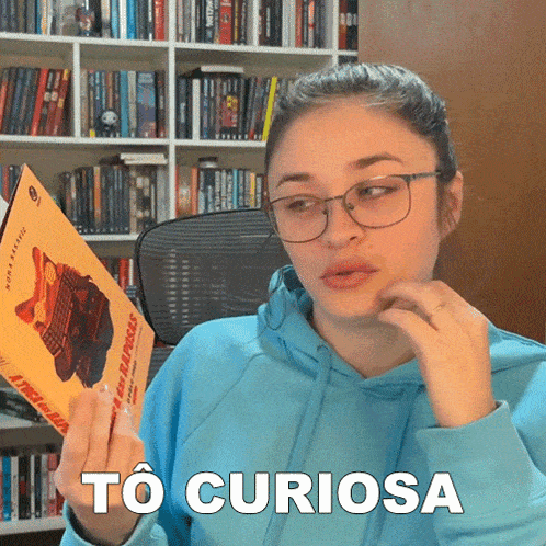 a woman in a blue hoodie holds a book in her hand and says to curiosa