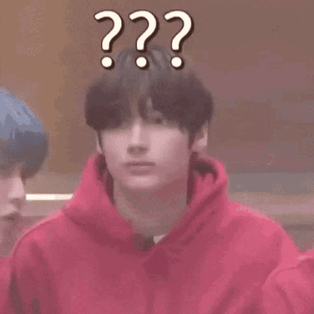a young man wearing a red hoodie is making a funny face with a question mark above his head .