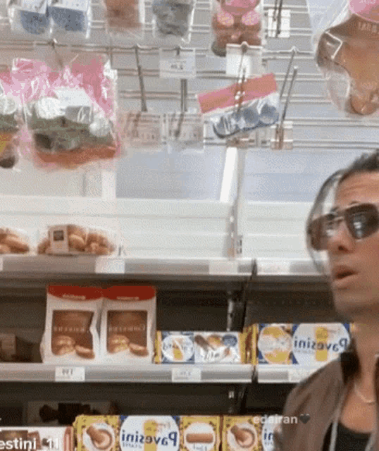 a man wearing sunglasses is standing in front of a shelf with boxes of initiatives on it