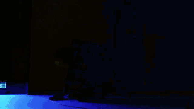 a person is kneeling down in a dark room with a blue light behind them .