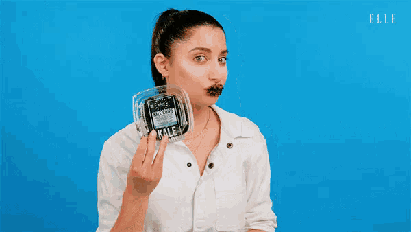 a woman holds a plastic container of kale chips in front of her face