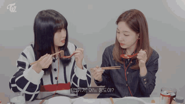 two girls are sitting at a table eating with chopsticks and the word twice is on the bottom of the screen