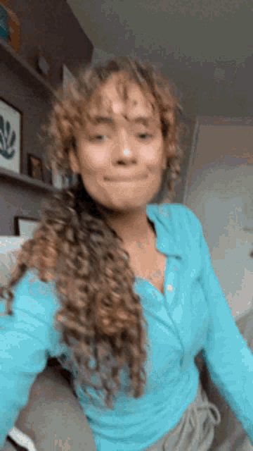 a woman with curly hair wearing a blue shirt is sitting on a couch