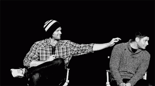 two men are sitting next to each other in chairs and one of them is touching the other 's face .