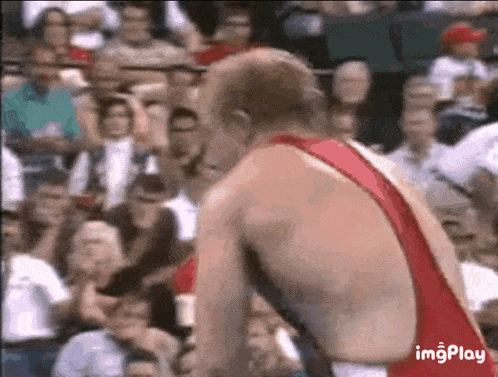 a wrestler in a red singlet is standing in front of a crowd .
