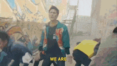 a man in a colorful jacket is standing in front of a wall with the words we are written on it .