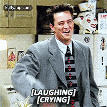a man in a suit and tie is laughing and crying while standing in a kitchen .