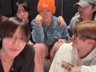 a group of young men are sitting next to each other and looking at the camera . one of the men is wearing an orange hat .