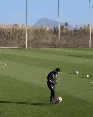 a man kicking a soccer ball on a field with mountains in the background
