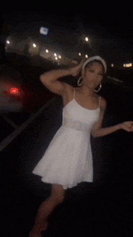 a woman in a white dress is dancing in a parking lot at night