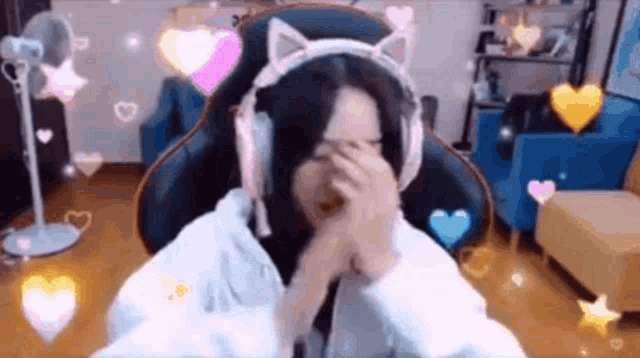 a woman wearing headphones is covering her face while sitting in a gaming chair .