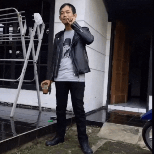 a man in a leather jacket smoking a cigarette and holding a cup of coffee
