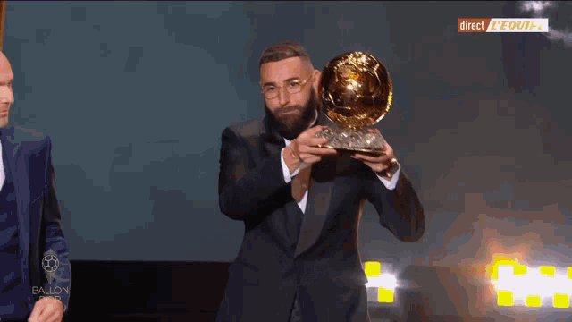 a man in a suit holds a trophy in front of a screen that says direct equipe