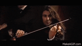 a man with long hair is playing a violin in front of a crowd .