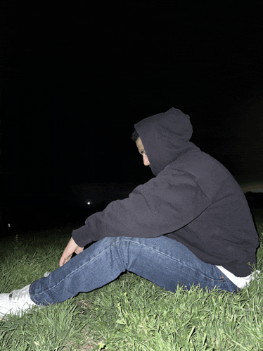 a person in a black hoodie sits in the grass