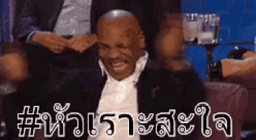 a man in a suit is sitting in a chair with his hands on his head and smiling .