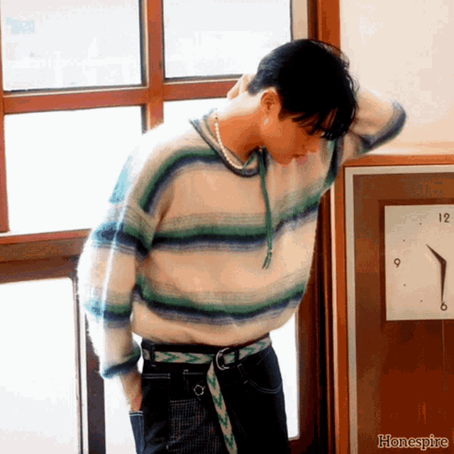a man wearing a striped sweater stands in front of a clock that says honeyspire on the bottom