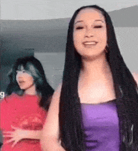 two women are standing next to each other in a room and one of them is wearing a purple top .