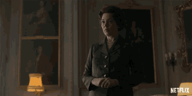 a woman in a suit and pearls stands in front of a netflix ad