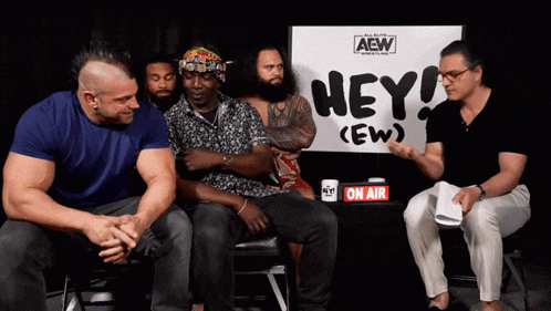 a group of men sit in front of a sign that says hey ew