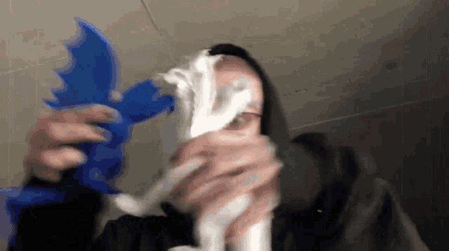 a man in a hoodie is holding a blue toy and a roll of toilet paper in front of his face .