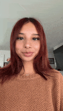 a woman with red hair is wearing a brown sweater and a necklace