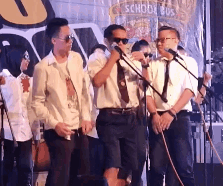 a group of men are singing into microphones in front of a school bus sign