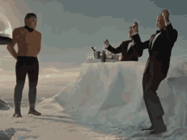 a man in a tuxedo is standing in the snow while two other men toast