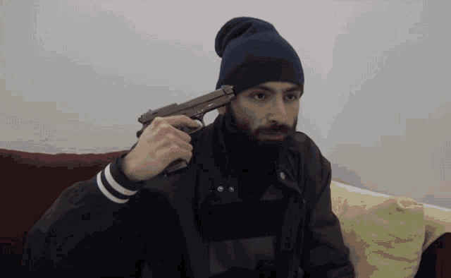 a man with a beard is holding a gun to his forehead