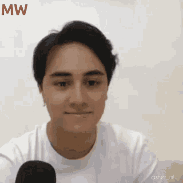 a man wearing a white shirt is talking into a microphone with the letters mw above his head