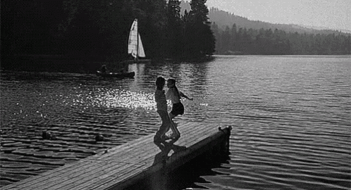 a couple is dancing on a dock next to a lake .