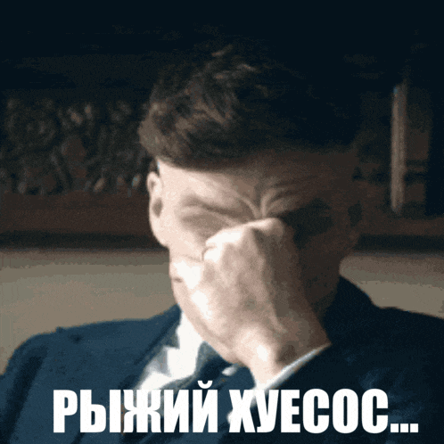 a man in a suit and tie is covering his face with his hand and the words " рыжий хуесос " are below him