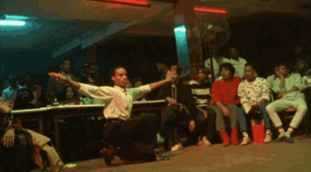 a man is kneeling on the floor in front of a crowd of people