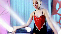 a little girl in a red heart shaped top is dancing on stage