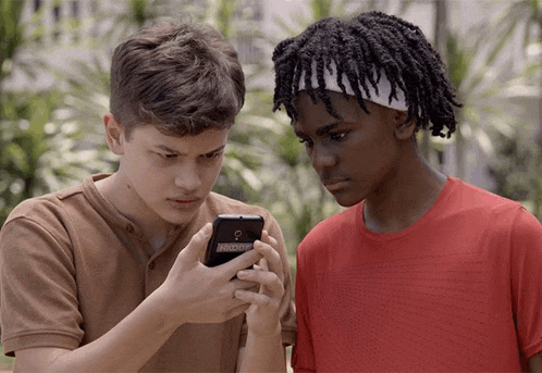 two boys are looking at a cell phone and one has a headband on his head that says ' reebok '