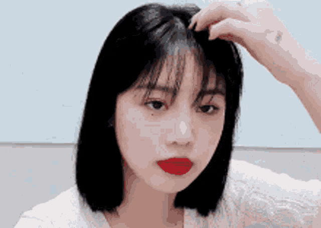 a woman with short black hair and red lipstick is holding her hair in her hand .