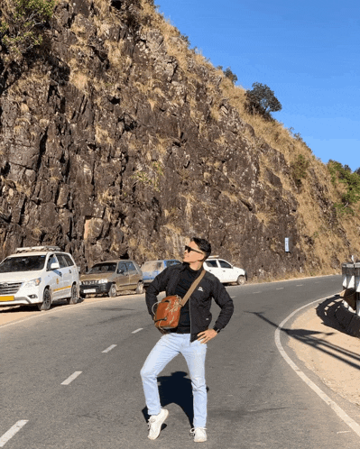 a man standing on the side of a road holding a bag