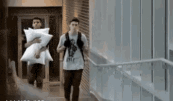 two men are carrying pillows in a hallway and one of them is wearing a shirt that says ' htc '