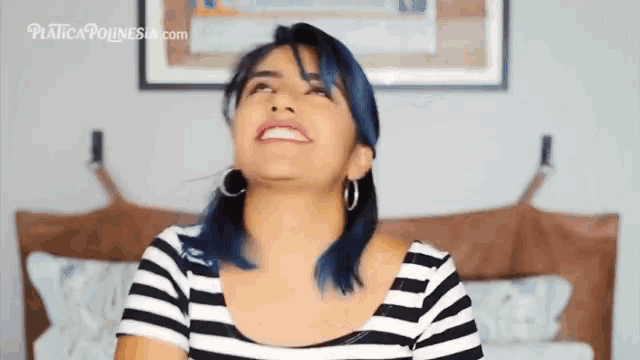 a woman with blue hair wearing a striped shirt and hoop earrings is smiling and looking up ..