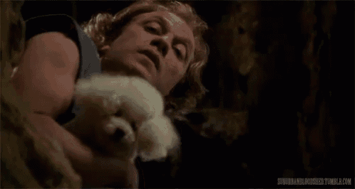 a man is holding a small white dog in his arms and licking it .